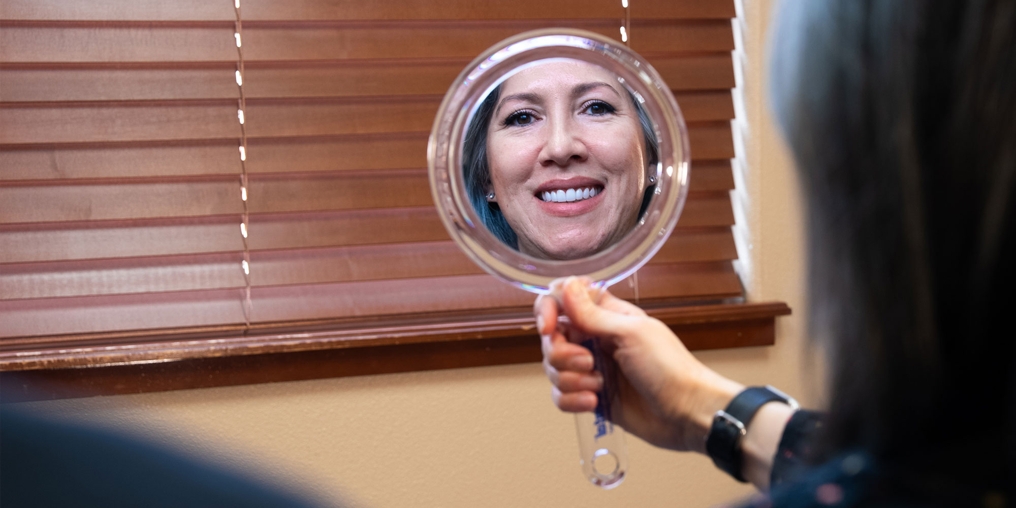 patient smiling brightly while holding a mirror
