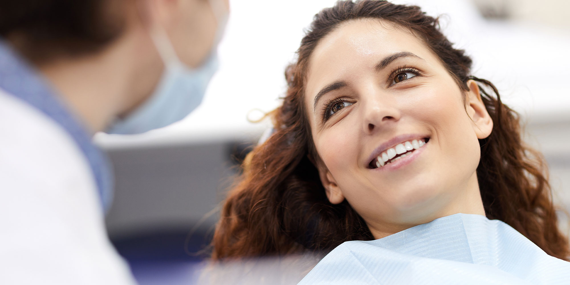 portrait of smiling young woman lying in dental chair and looking at doctor